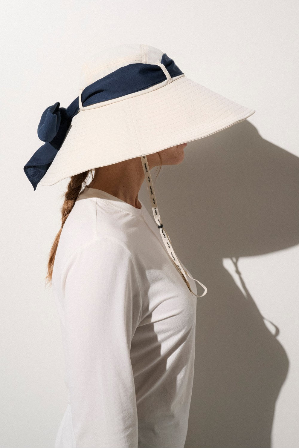 Chapeau anti-UV femme blanc, avec large bord pour une très haute protection solaire, porté avec un ruban bleu marine.
