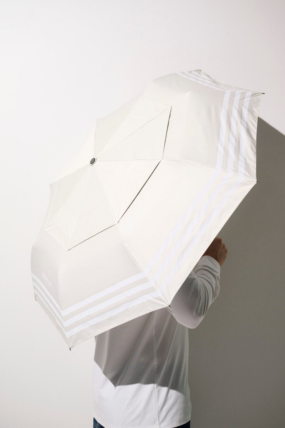 Ombrelle anti-UV - Pornichet, homme tenant un parapluie beige léger avec rayures, protection solaire efficace.