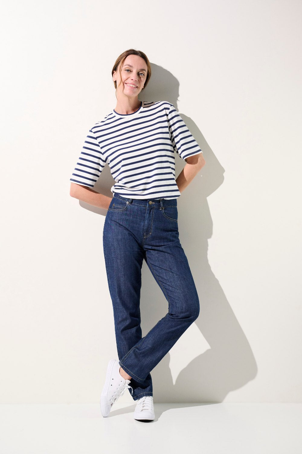 Femme portant un t-shirt à rayures et un jean bleu, style décontracté, mode élégante pour tous les jours.