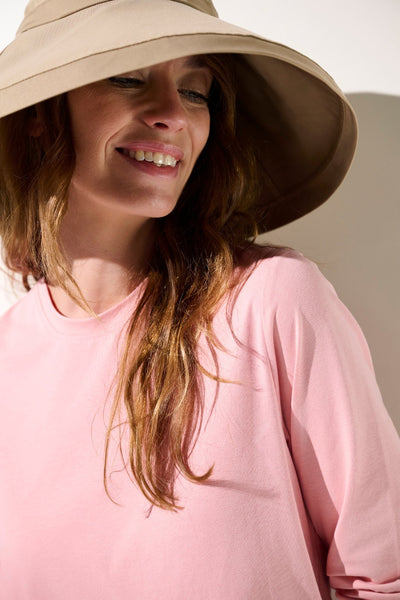 Femme souriante portant un chapeau anti-UV - Faro beige et un t-shirt rose, protection solaire UPF 50+.
